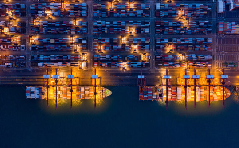 Aerial top view of container cargo ship in the export and import business and logistics international goods in urban city. Shipping to the harbor by crane in Victoria Harbour, Hong Kong City at night