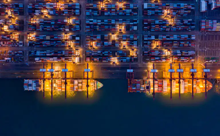 Aerial top view of container cargo ship in the export and import business and logistics international goods in urban city. Shipping to the harbor by crane in Victoria Harbour, Hong Kong City at night
