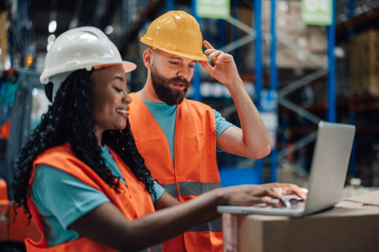 Multiracial man and woman collaborating on laptop for warehouse tasks